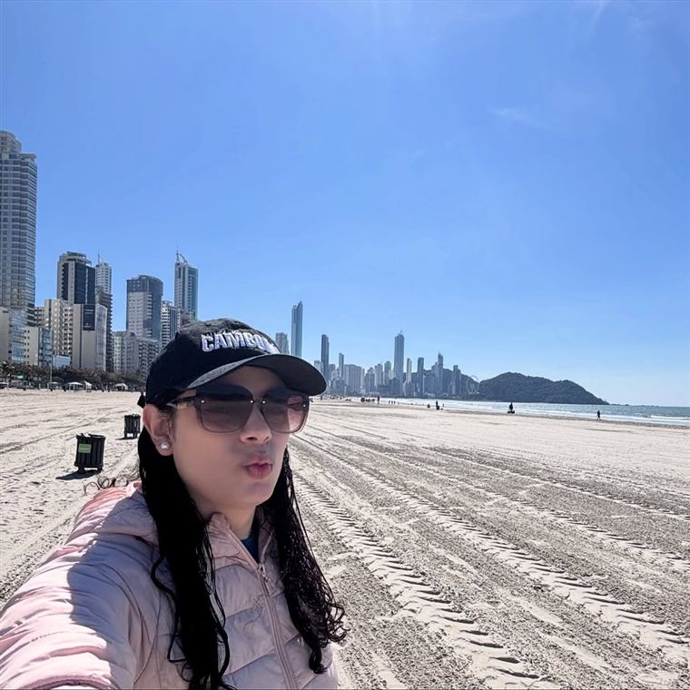 Nicole em uma praia com prédios ao fundo